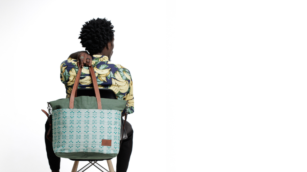 Person sitting on a chair with a green patterned bag, holding a baby